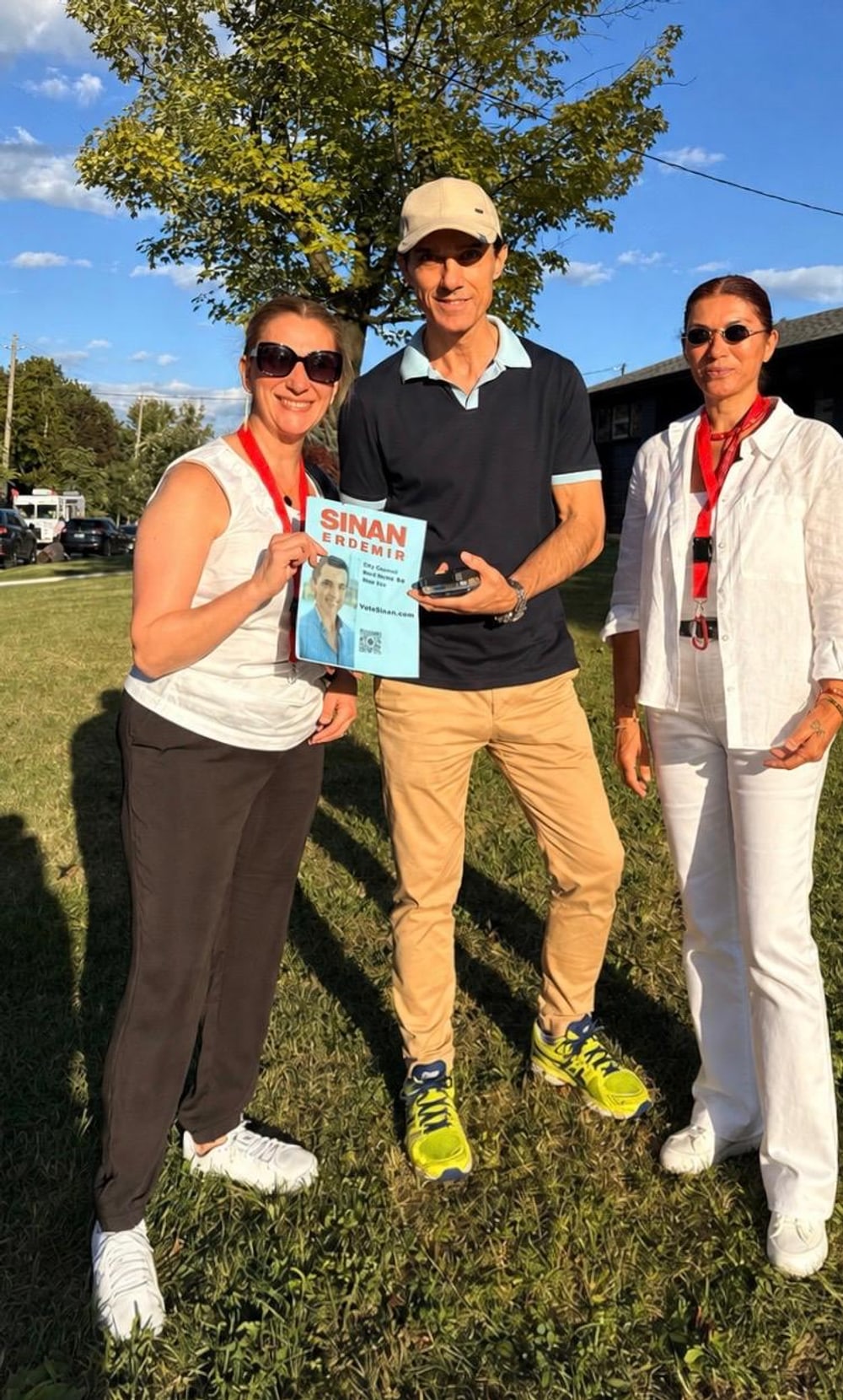 Sinan Erdemir with two supporters holding a campaign flyer at a neighbourhood event
